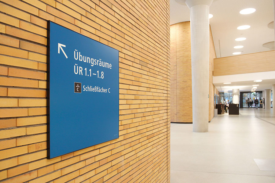 Wegweiser zu den Übungsräumen auf einer Klinkerfassade